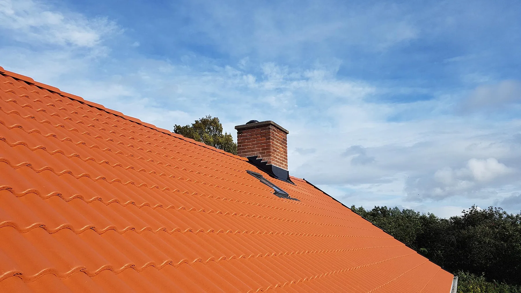 Tegeltak med skorsten och plåtbeslag mot blå himmel